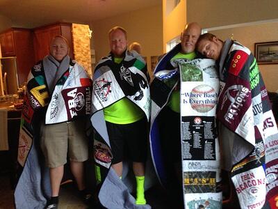 A group of 4 adult brothers wrapped in their T-shirt quilts as seen from the font by Too Cool T-shirt Quilts